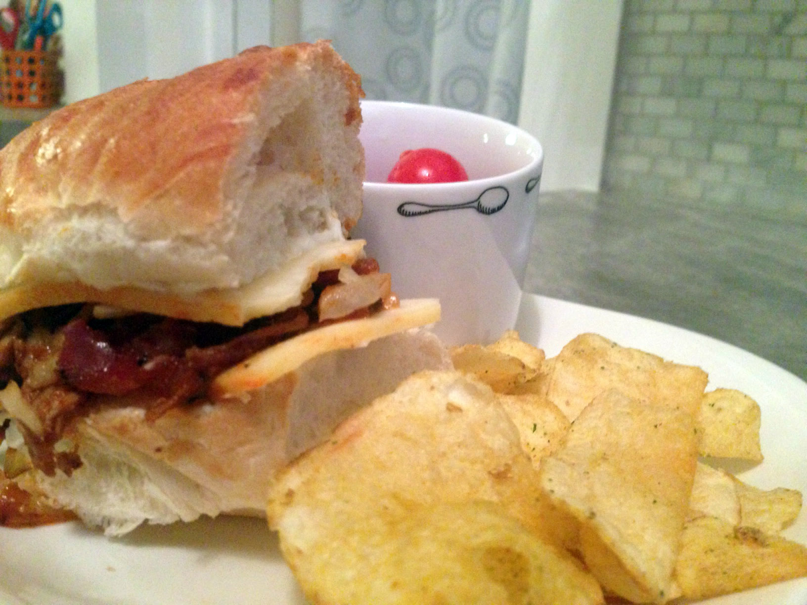 Image of leftover pulled pork turned into sandwich; with chips and baby tomatoes