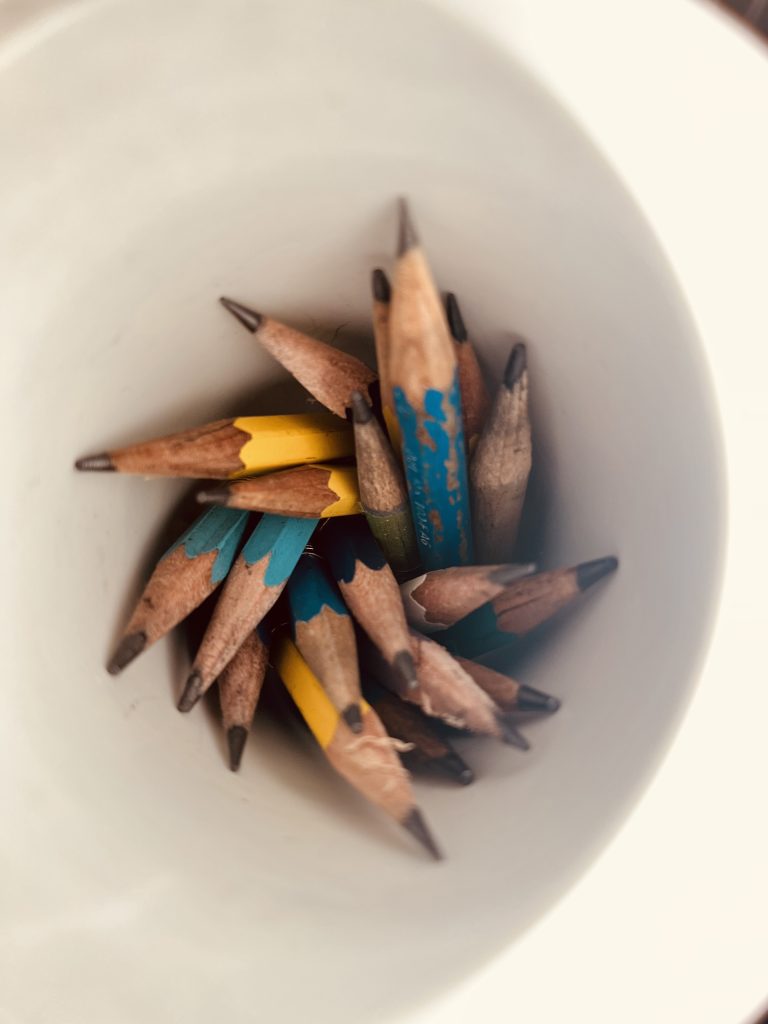 Small sharpened pencils tucked into a white cup.